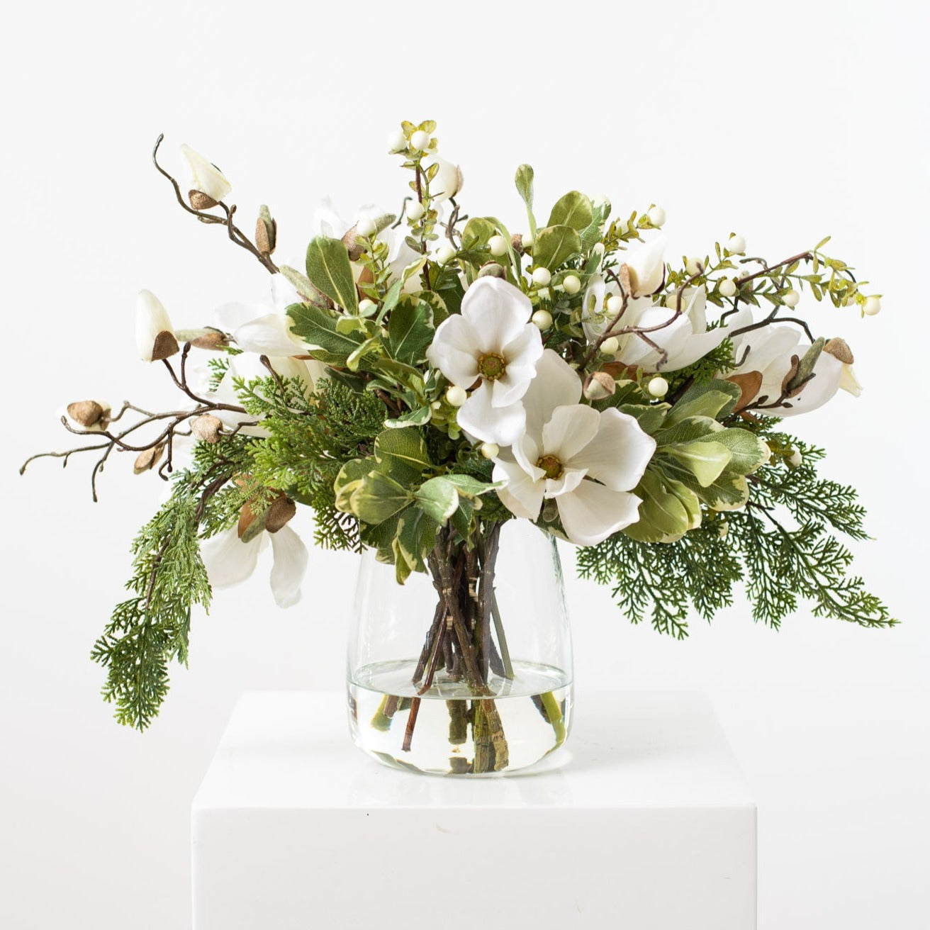 https://darbycreektrading.com/cdn/shop/products/WhiteMagnolia_MixedGreens_BerryEverydayWinterFloralArrangementCenterpieceinTaperedGlassVase2_1800x1800.jpg?v=1698866042